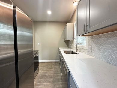 Kitchen with stainless steel appliances, gray cabinetry, light stone counters, dark wood finished floors, and backsplash