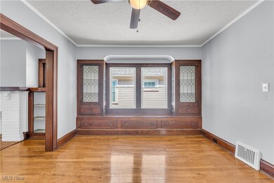 Empty room with a ceiling fan, crown molding, light wood finished floors, and visible vents