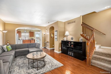 Living area with arched walkways, stairs, dark wood finished floors, and ornamental molding