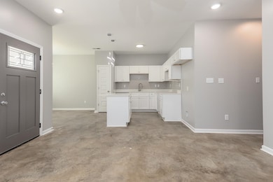 Kitchen with concrete floors, white cabinetry, a kitchen island, tasteful backsplash, and light countertops