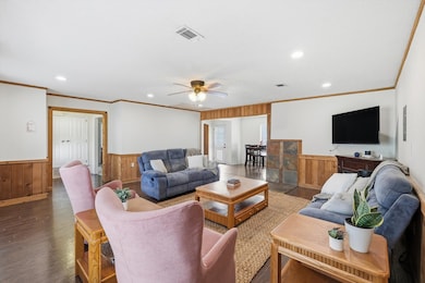 Living area with crown molding, wood walls, wainscoting, wood finished floors, and a ceiling fan