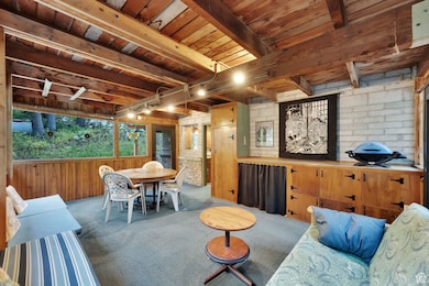 Carpeted enclosed deck featuring a wooden ceiling with exposed beams, rail lighting, and wooden walls