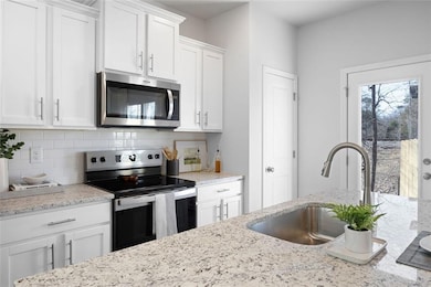 Kitchen with a sink, stainless steel appliances, decorative backsplash, white cabinets, and light stone countertops