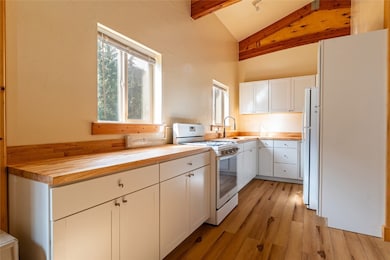 Kitchen with white cabinets, butcher block countertops, white appliances, and light wood-style flooring