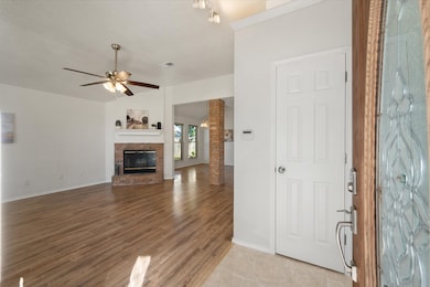 Unfurnished living room with a textured ceiling, ceiling fan, a brick fireplace, and light wood-type flooring
