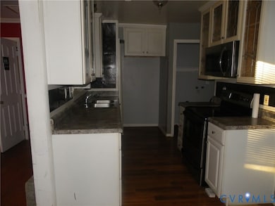 Kitchen with black electric range, stainless steel microwave, dark countertops, and white cabinetry