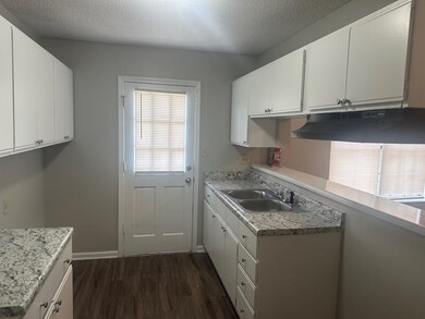 Kitchen featuring under cabinet range hood, dark wood-style flooring, white cabinets, and a textured ceiling