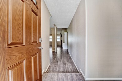 A solid mahogany paneled front door opens from the front porch to reveal neutral paint and wood-look laminate flooring with the family room straight ahead and an arched entrance into a flex-use dining or office space on the left.