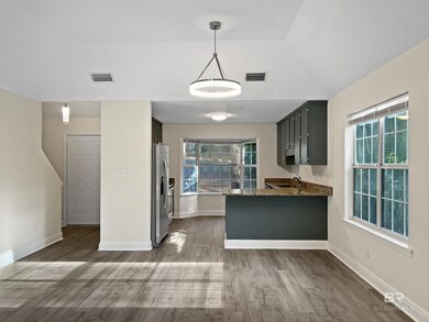 Kitchen with dark stone countertops, light wood finished floors, a peninsula, stainless steel fridge, and decorative light fixtures