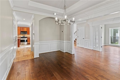dining area with a chandelier, light wood-style flooring, a raised ceiling, a decorative wall.