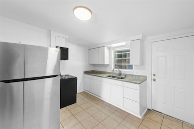 Kitchen with freestanding refrigerator, light stone countertops, white cabinets, and light tile patterned floors