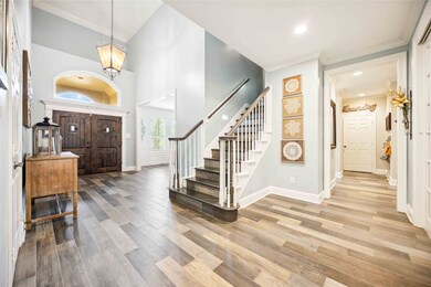 Home entrance with wood-look tile floor, staircase, and wooden double doors under an arched alcove.