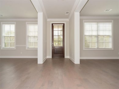 Entrance foyer featuring dark wood-type flooring, visible vents, ornamental molding, and baseboards