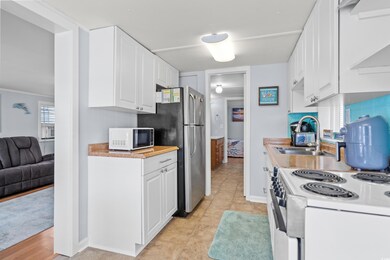 Kitchen featuring white appliances, a sink, white cabinets, light countertops, and baseboards