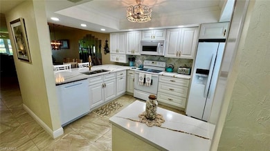 Kitchen with white appliances, a chandelier, a sink, a textured wall, and crown molding