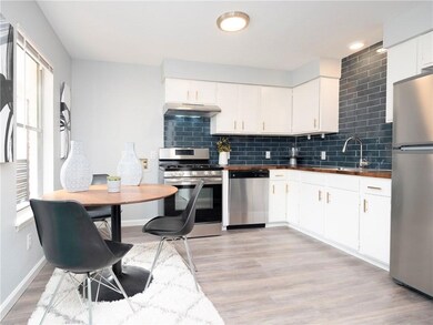 Kitchen with decorative backsplash, appliances with stainless steel finishes, white cabinets, light wood-type flooring, and dark countertops
