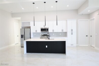 Kitchen featuring appliances with stainless steel finishes, decorative backsplash, light stone countertops, white cabinetry, and a kitchen island with sink