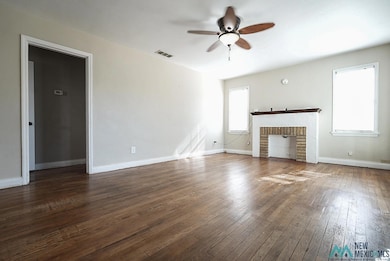 Unfurnished living room featuring healthy amount of natural light, dark wood finished floors, ceiling fan, and a fireplace