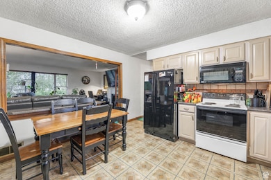 Kitchen featuring black appliances, decorative backsplash, a textured ceiling, open floor plan, and dark stone counters