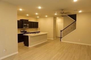 Kitchen featuring light hardwood / wood-style flooring, a kitchen island with sink, ceiling fan, decorative backsplash, and stove
