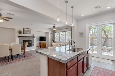 Kitchen with french doors, decorative light fixtures, light stone counters, open floor plan, and a glass covered fireplace