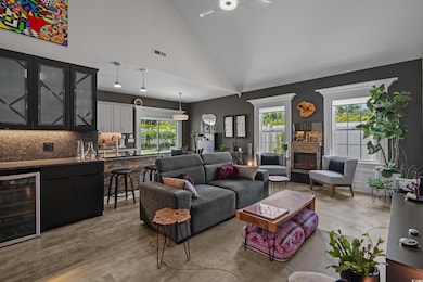 Living area featuring beverage cooler, plenty of natural light, ceiling fan, a lit fireplace, and high vaulted ceiling