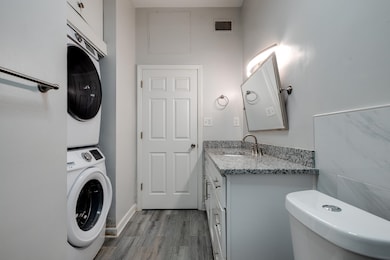 Half bath featuring stacked washer / dryer, wood finished floors, toilet, and vanity
