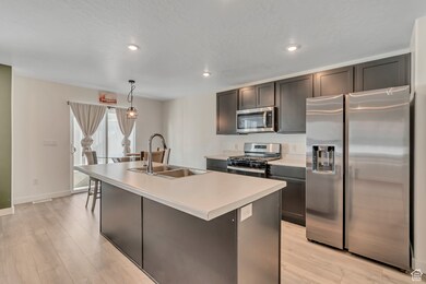 Kitchen featuring stainless steel appliances, light countertops, a kitchen island with sink, decorative light fixtures, and recessed lighting