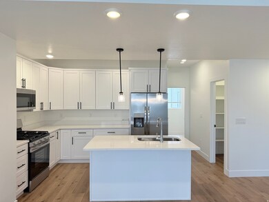 Kitchen featuring stainless steel appliances, decorative pendant lights, laminate wood floors, a center island with sink, and quartz counters