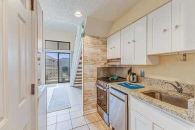 Kitchen featuring a textured ceiling, white cabinetry, light tile patterned flooring, appliances with stainless steel finishes, and light stone counters