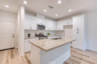 Kitchen with breakfast bar island, Stainless Steel gas range and microwave, quartz counters, white subway tile backsplash and custom cabinetry.
