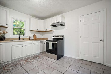 Kitchen with electric stove, under cabinet range hood, white cabinetry, a textured ceiling, and light countertops