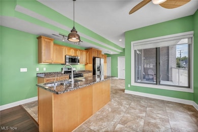 Kitchen featuring sink, hanging light fixtures, appliances with stainless steel finishes, dark stone countertops, and ceiling fan