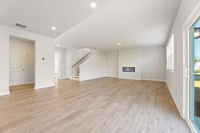 Unfurnished living room featuring visible vents, stairway, a glass covered fireplace, light wood-style floors, and recessed lighting