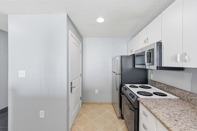 Kitchen featuring stainless steel appliances, a textured ceiling, white cabinets, light tile patterned floors, and light stone countertops