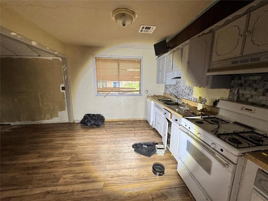 Kitchen with white appliances, light wood-type flooring, backsplash, under cabinet range hood, and white cabinets