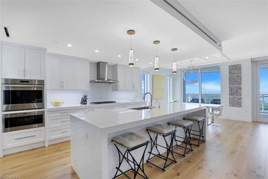 Kitchen featuring stainless steel double oven, a breakfast bar, an island with sink, wall chimney range hood, and backsplash
