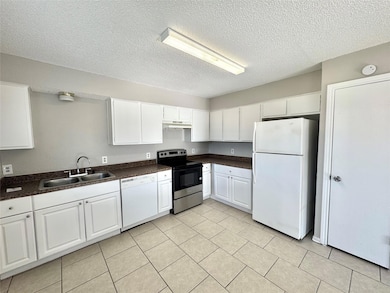 Kitchen featuring white cabinetry, white appliances, light tile patterned floors, a textured ceiling, and sink