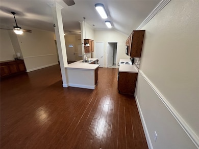 Kitchen featuring crown molding, light countertops, dark wood-style floors, lofted ceiling, and a peninsula