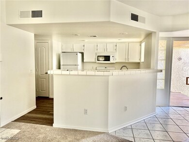 Kitchen with tile counters, white appliances, white cabinets, and a peninsula