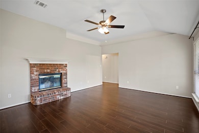 Unfurnished living room with a fireplace, dark wood finished floors, vaulted ceiling, and ceiling fan