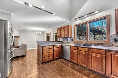 Kitchen with appliances with stainless steel finishes, brown cabinets, backsplash, ornamental molding, and a chandelier