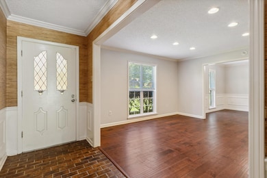 Entrance foyer featuring a textured ceiling, crown molding, a wainscoted wall, a decorative wall, and dark wood-style flooring