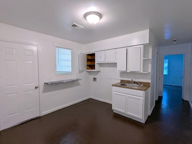 Kitchen featuring a sink, visible vents, white cabinetry, baseboards, and concrete floors