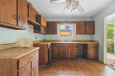 Kitchen featuring dark wood-style floors, a ceiling fan, light countertops, and brown cabinets