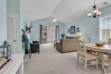 Dining space featuring light carpet, vaulted ceiling, a ceiling fan, and a chandelier