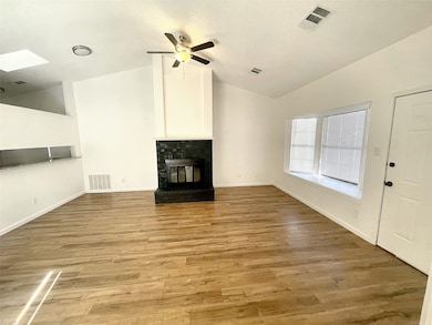 Unfurnished living room featuring vaulted ceiling, light wood-type flooring, a fireplace, a skylight, and a ceiling fan
