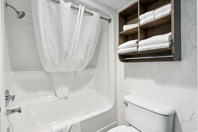 Bathroom featuring toilet, washtub / shower combination, tile walls, and decorative backsplash