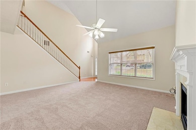 Unfurnished living room featuring high vaulted ceiling, light carpet, a fireplace with flush hearth, a ceiling fan, and stairway