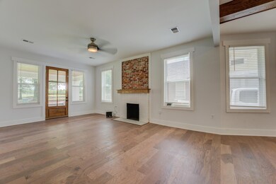 Unfurnished living room with ceiling fan, baseboards, wood finished floors, and a brick fireplace
